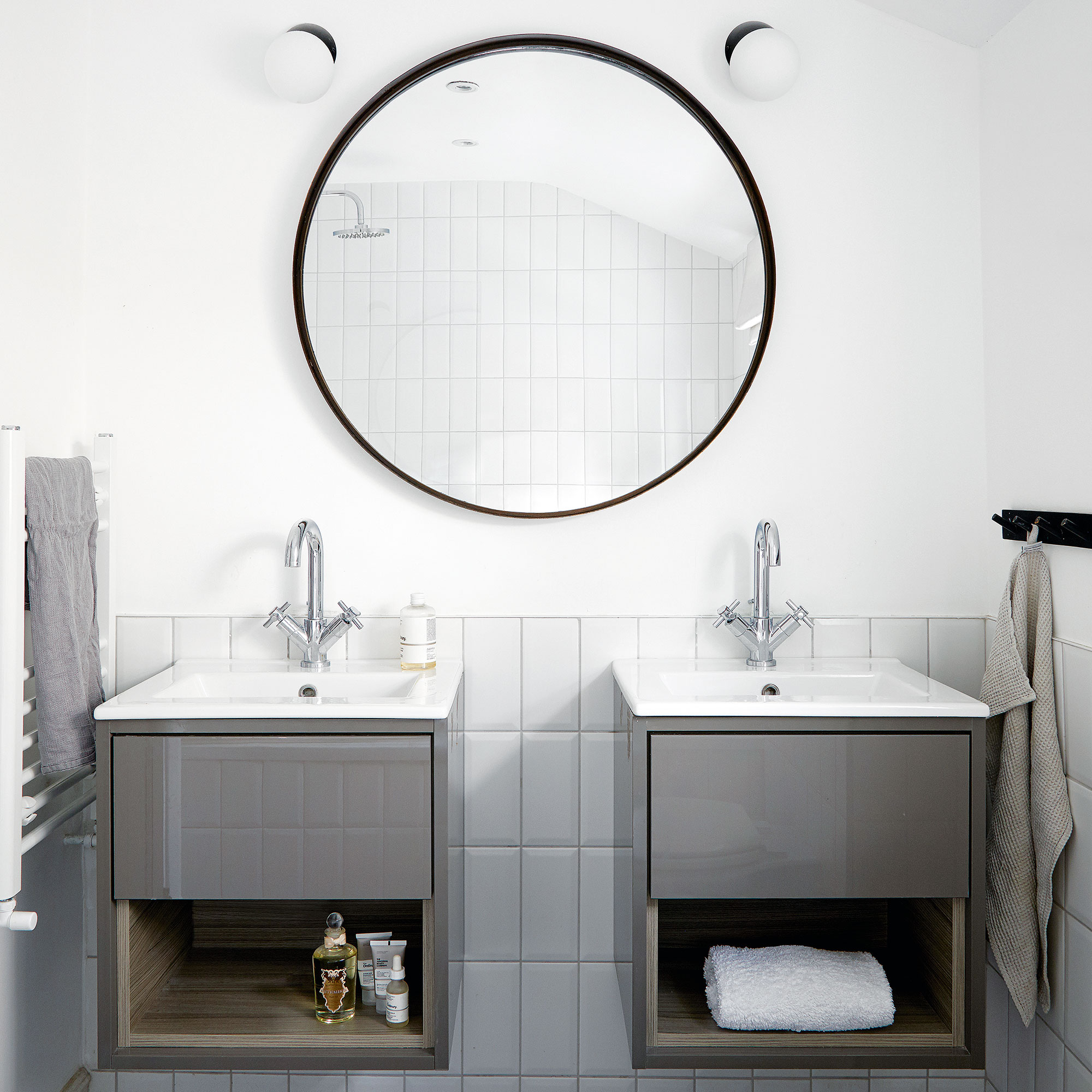White bathroom with two grey vanity units beneath round mirror