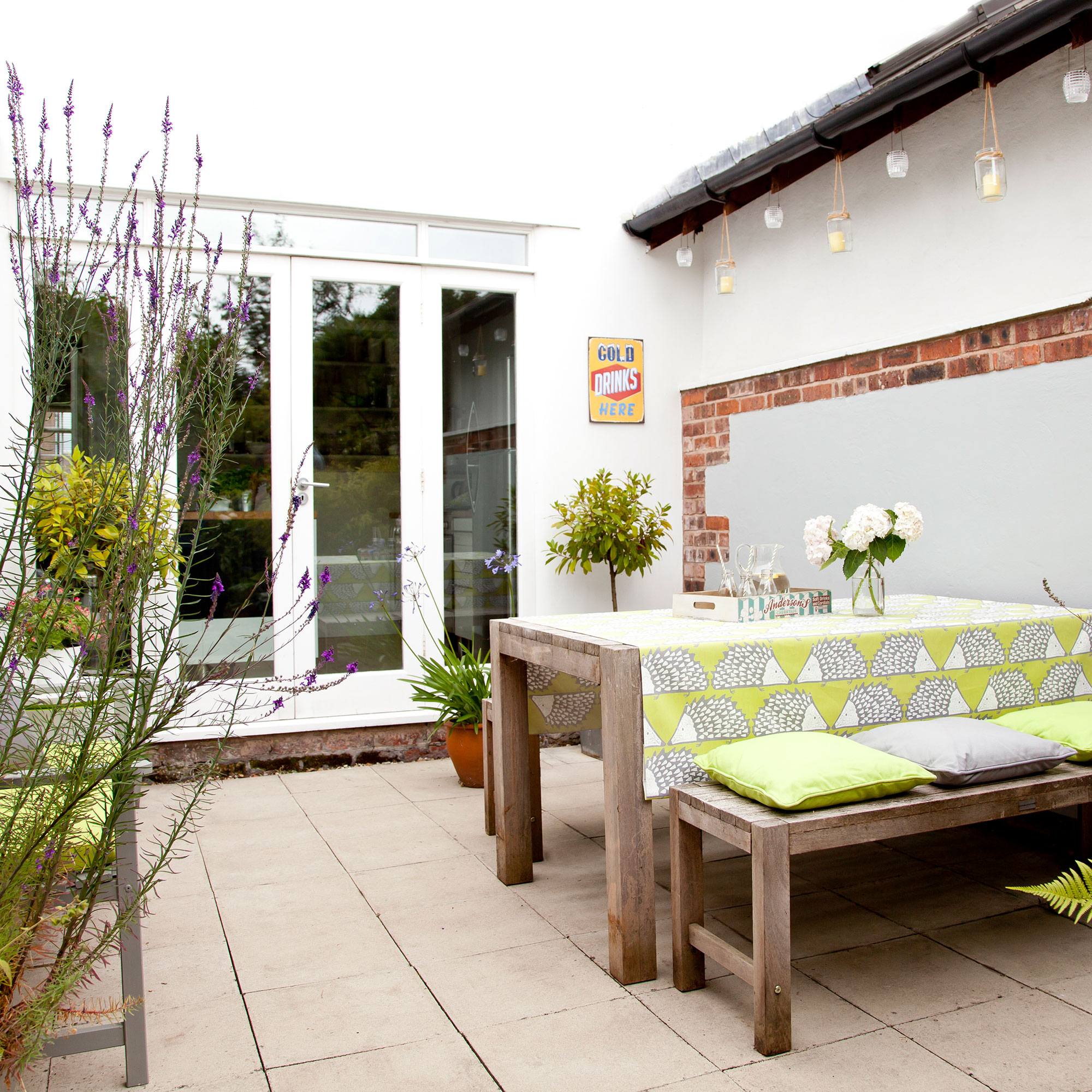 Courtyard garden, by wooden garden bench and table with lime green patterned cloth and cushions, stone patio.