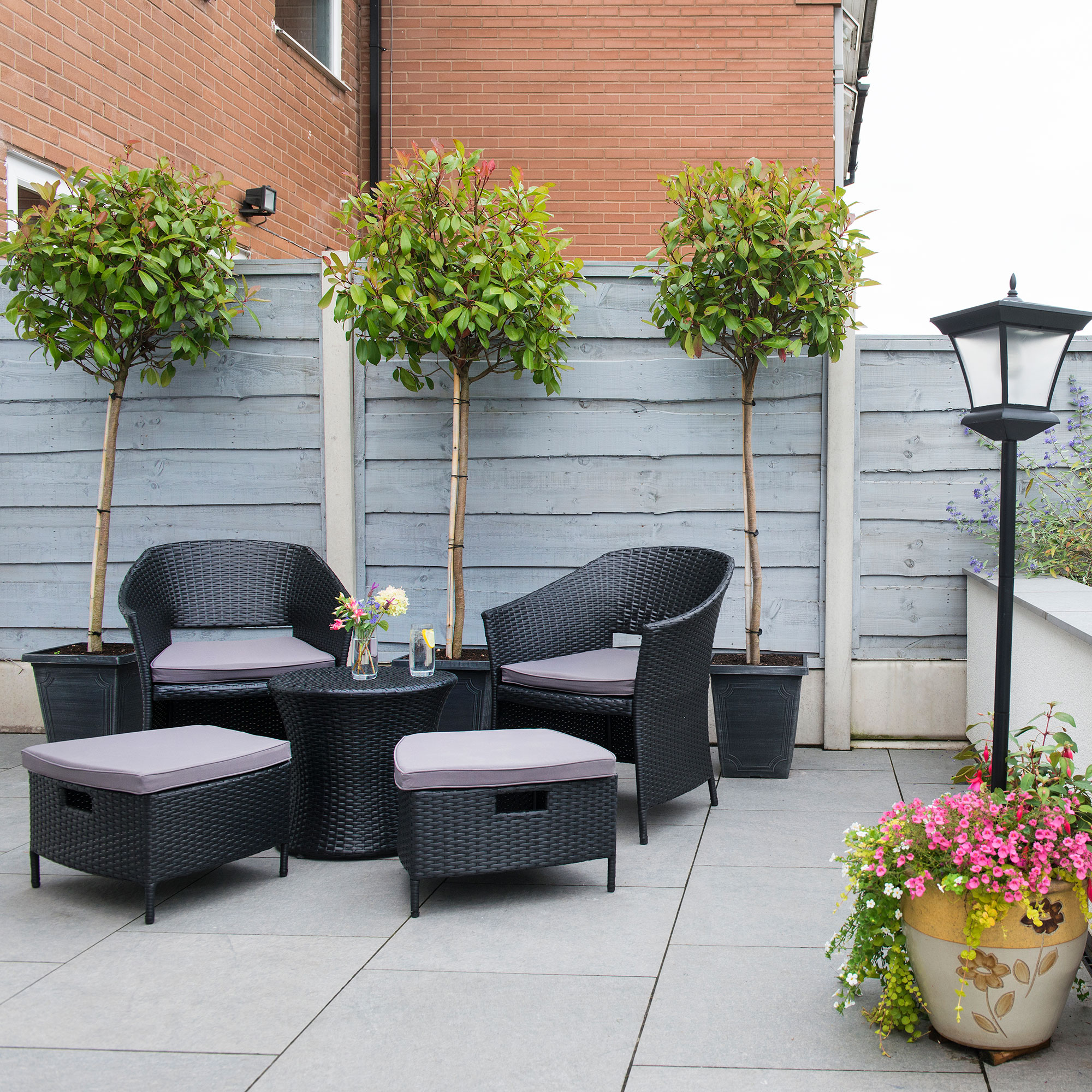 A redesigned low maintenance garden with hard landscape, Grey fencing and seats and a table, and a low wall.