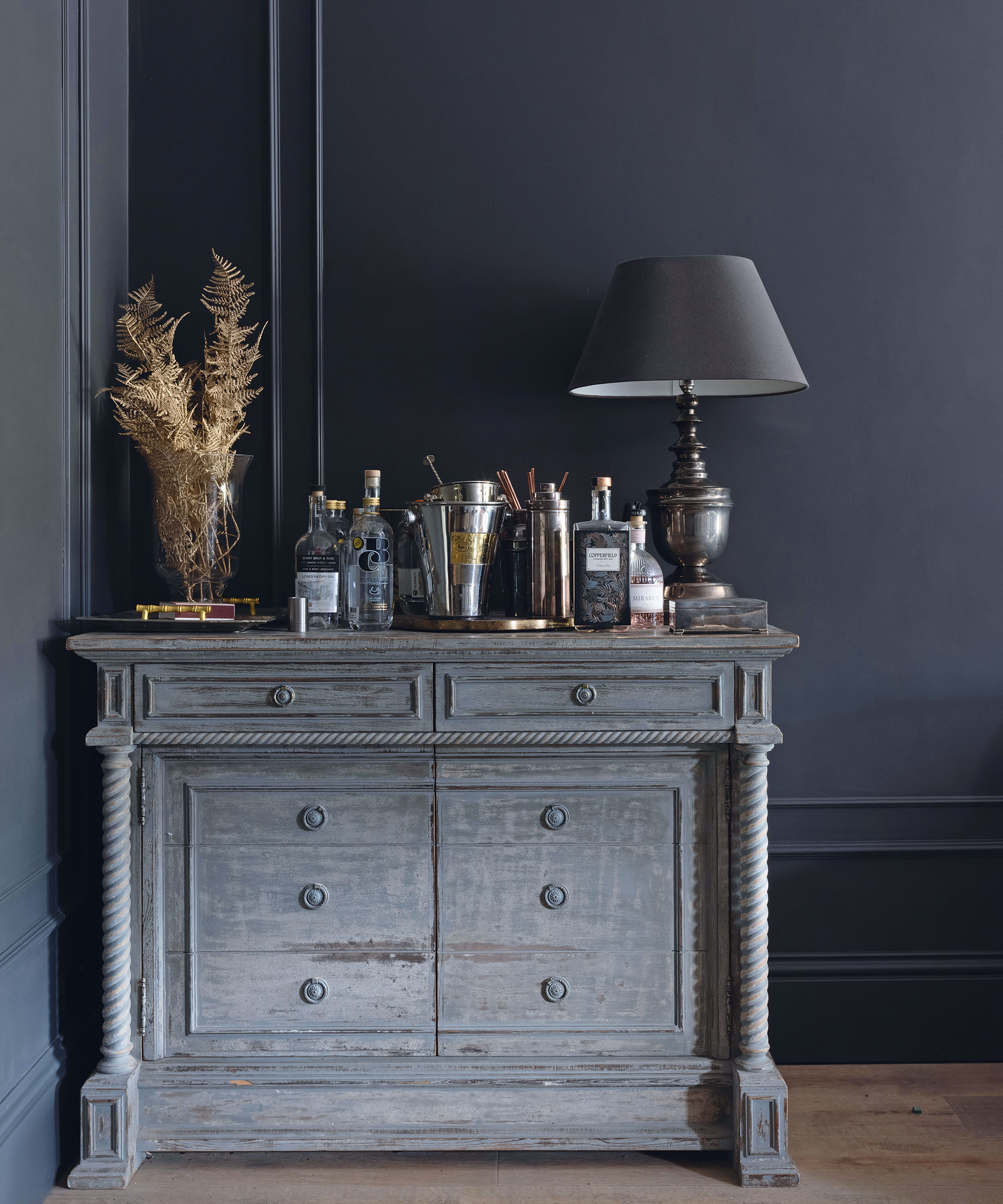 Sideboard topped with barware infront of dark grey painted panelled walls